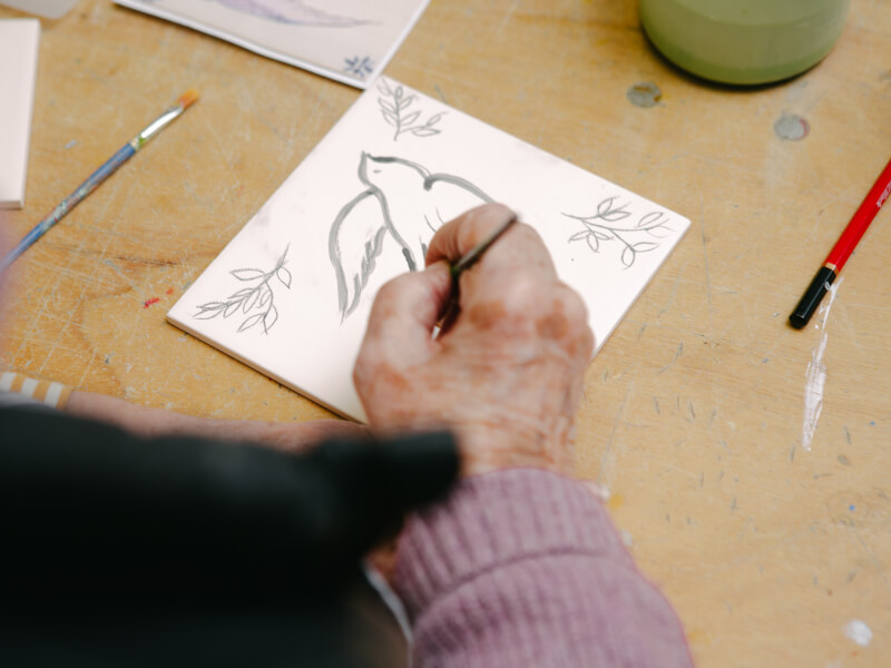 Elderly person's hand paiting a dove on a square tile